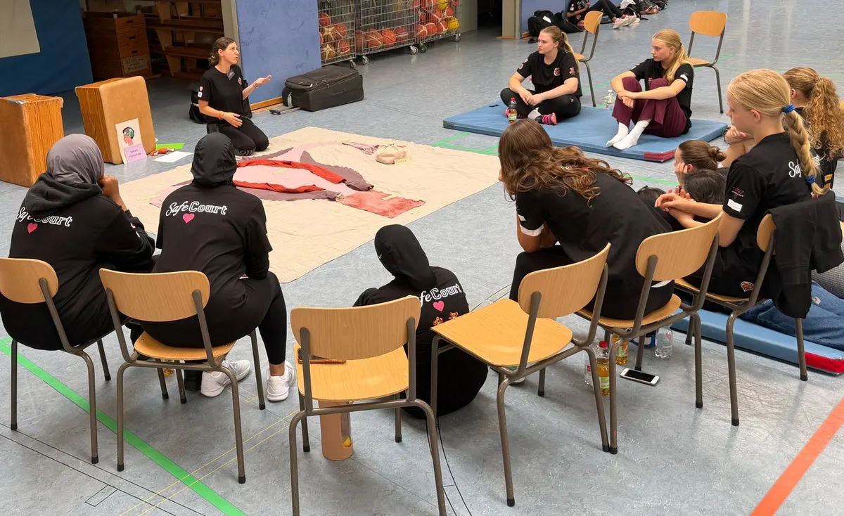Mädchen-Workshop in einer Turnhalle: die Teilnehmerinnen sitzen im Stuhlkreis um das Bodenbild, Anne sitzt gegenüber und erklärt