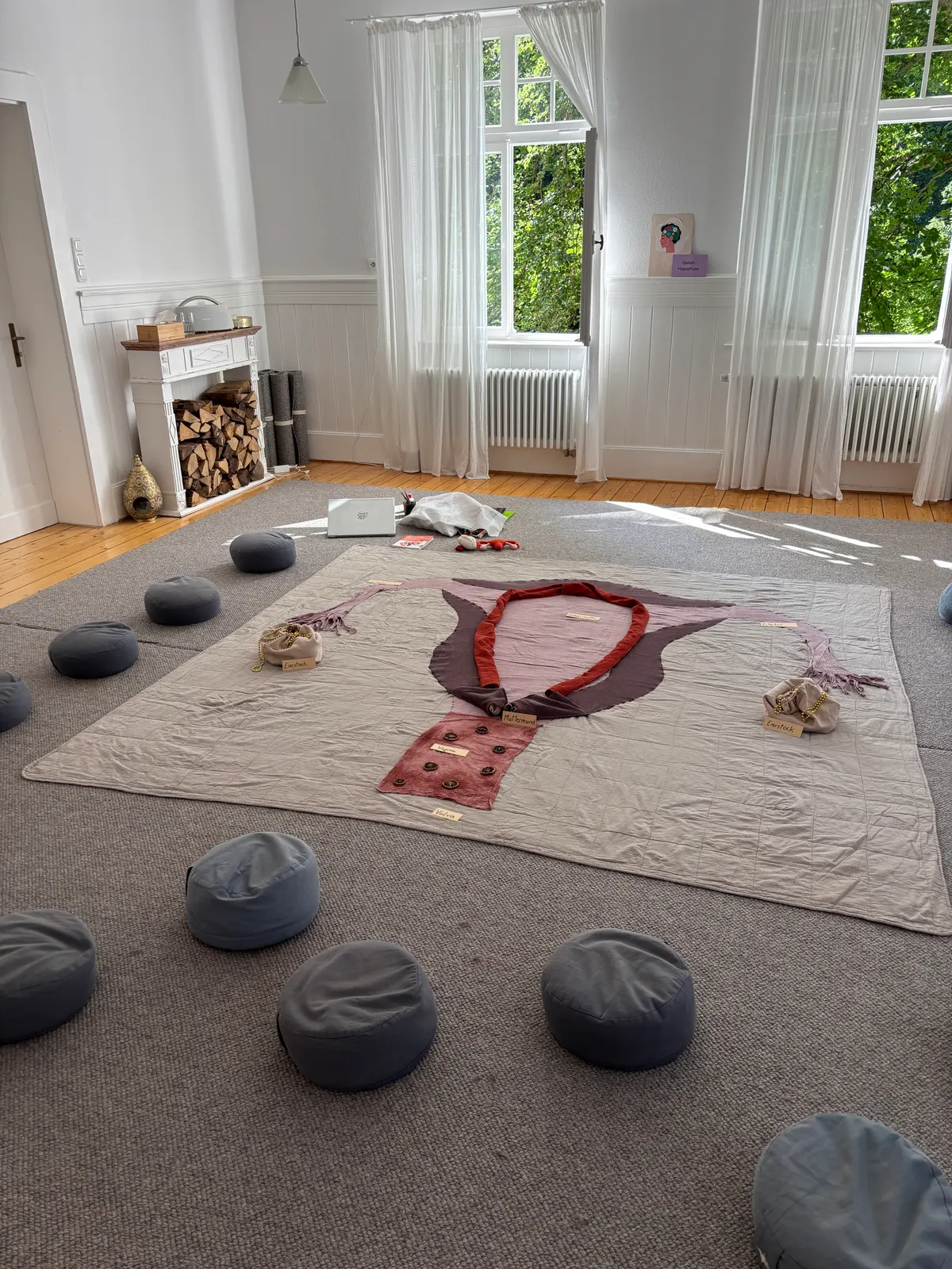 Das große Bodenbild liegt in einem hellen Altbauraum auf dem Teppich, ringsum graue Sitzkissen für die Teilnehmerinnen